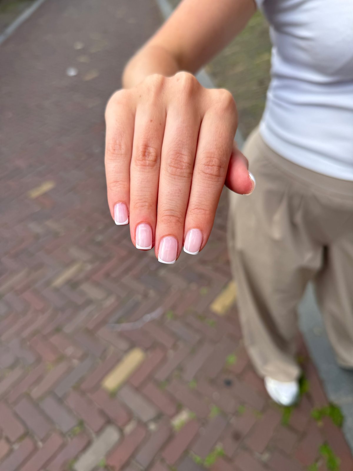 Hand met roze French nagels buiten op een visgraatbestrating