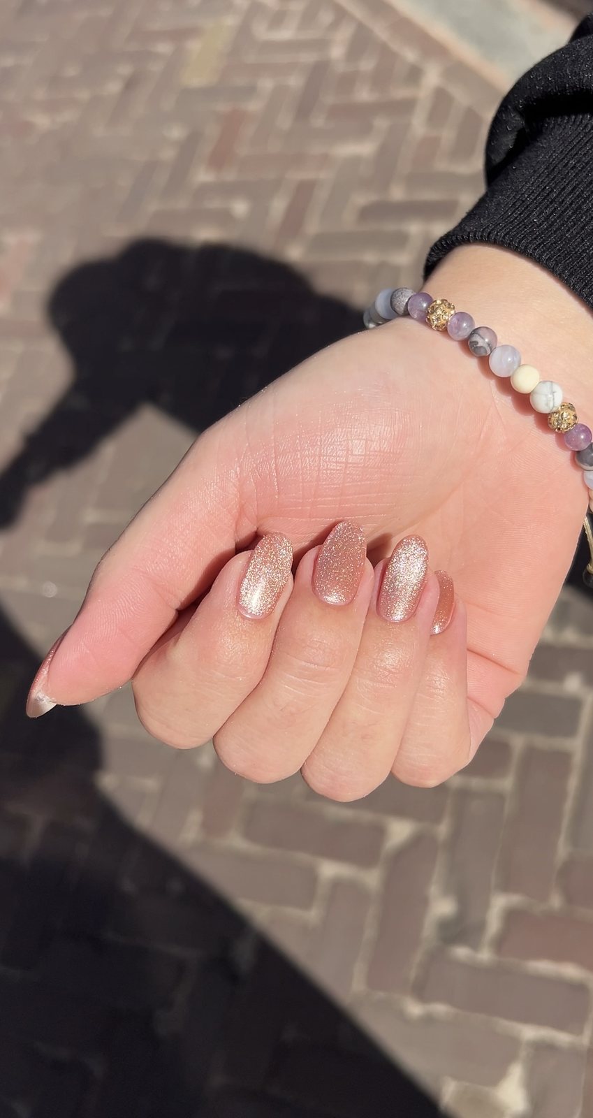Hand met melkroze chrome nagels boven klinkers