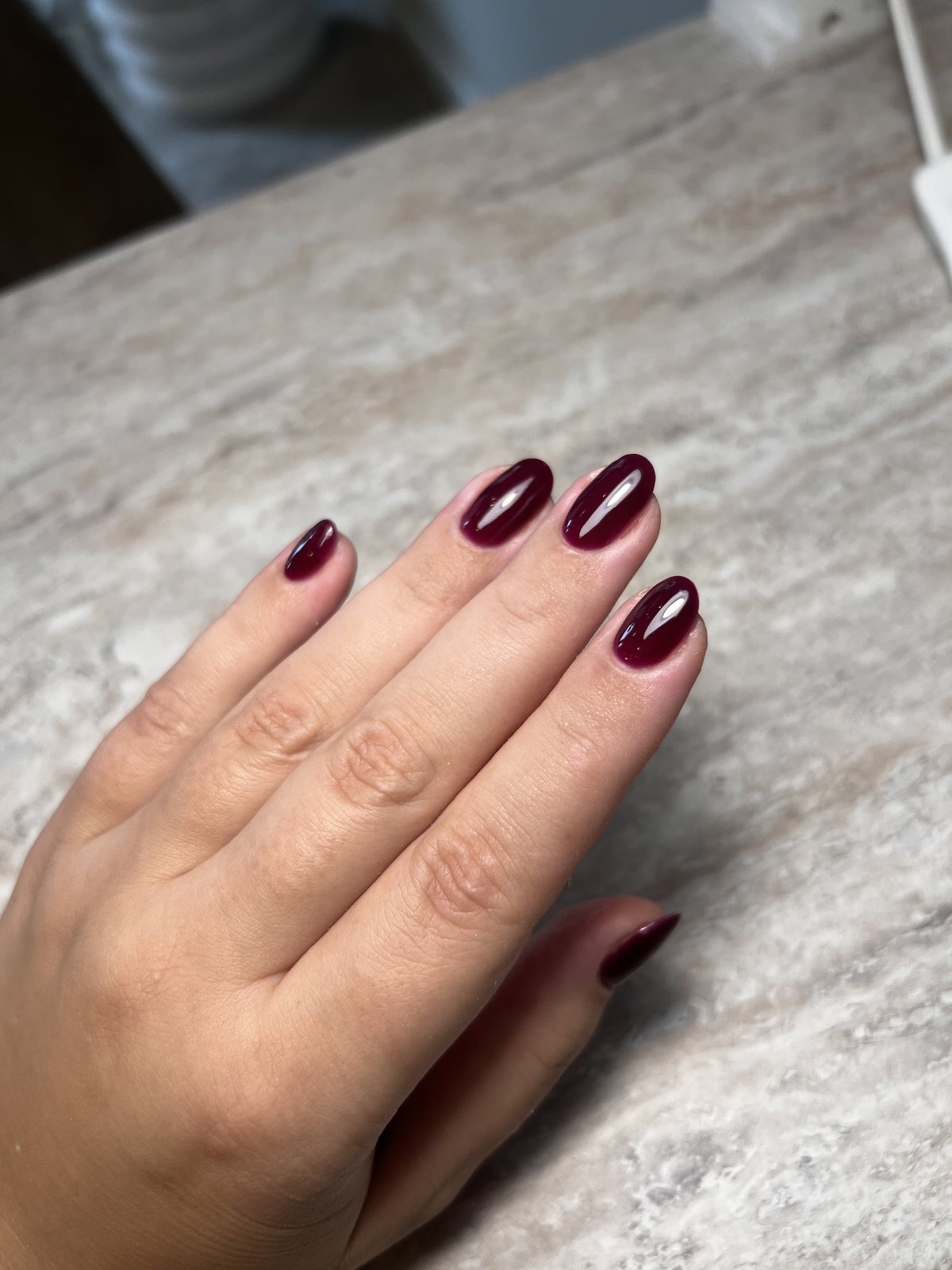 Hand met diep bordeauxrode nagels op een marmeren tafel