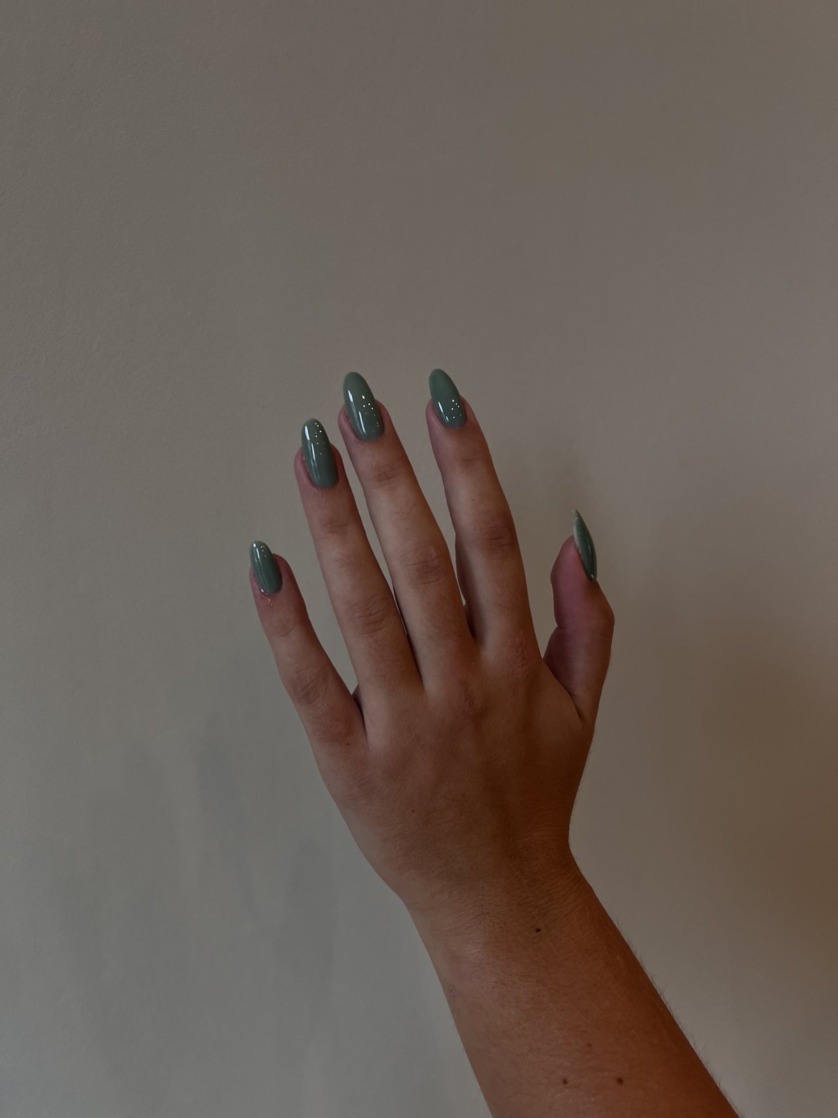 Hand met saliegroene nagels tegen een greige muur