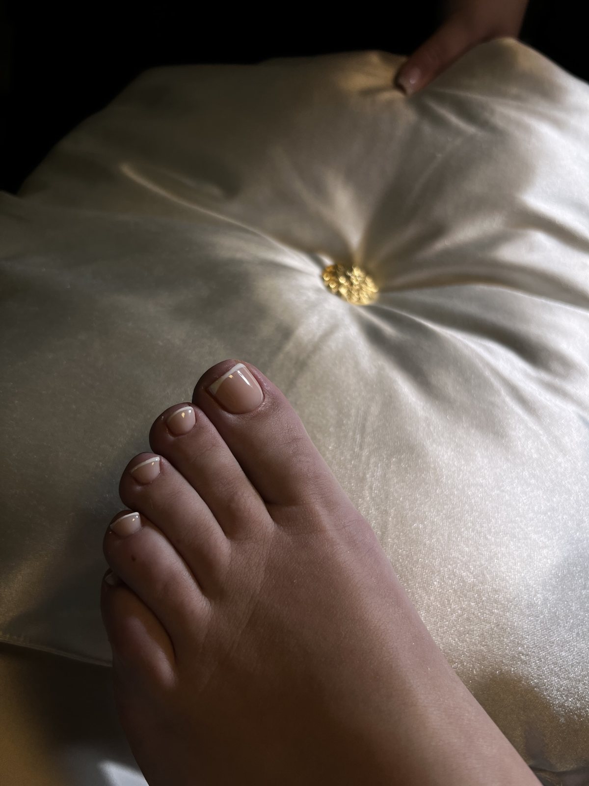 Voet met taupe gellak op de teennagels, op een satijnen kussen
